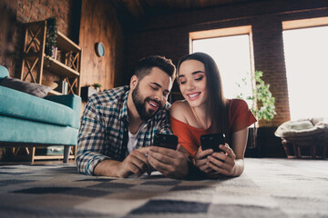 Poster - Full body photo of cheerful cute young couple lying floor device enjoy weekend have fun buy new apartment indoors inside house home