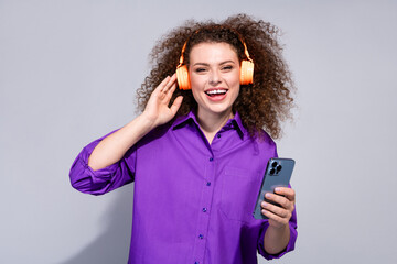 Wall Mural - Portrait of pretty young woman touch headphones hold phone wear violet shirt isolated on grey color background