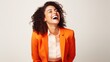 © Iona - A woman in a vibrant orange blazer laughs joyously against a soft ivory backdrop, exuding confidence and charisma.