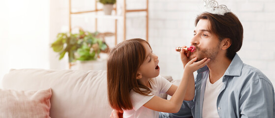 Wall Mural - Small girl putting lipstick on daddy lips at home, dad wearing crown, copy space