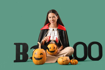 Poster - Young woman in Halloween costume and with pumpkins on green background