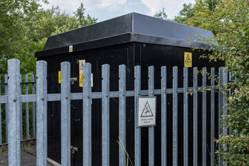 Black suburban electricity substation with galvanized metal fence, hedge, and danger keep out signs