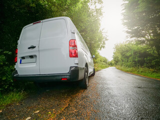 Wall Mural - A white medium size van is parked on a small county road in rural area with a red tail light. The road is empty and the sun is shining brightly. Product delivery to remote locations concept.
