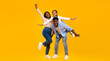 © Prostock-studio - Spending Time With Family Is Fun. Full body length of excited African American man, woman and girl laughing and posing isolated on yellow studio wall. Cheerful father carrying daughter on back, banner