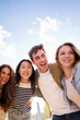 © CarlosBarquero - Vertical. Selfie portrait of young people group looking smiling at mobile camera sharing happy moment outdoors. Diverse generation z friends posing together under clear blue sky with fluffy clouds