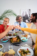 © CarlosBarquero - Vertical. Caucasian people of diverse generations gathered laughing toasting with white wine in meal reunion indoor. Cheerful family have fun with food event at home. Positive domestic relations