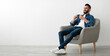 © Prostock-studio - Full length of young Arab man drinking hot coffee in armchair against white studio wall, banner with free space. Peaceful middle Eastern guy having relaxing day, chilling on lazy morning