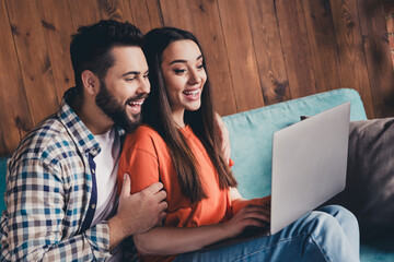 Canvas Print - Photo of cheerful cute young couple cuddle sit sofa eshopping enjoy weekend have fun buy new apartment indoors inside house home