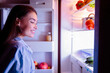 © Prostock-studio - Good night snack. Cheerful girl looking for food in fridge late in night, free space