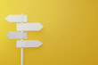 © Mrt - Minimalist white signpost with blank directional arrows against bright yellow background with empty copy space for text.