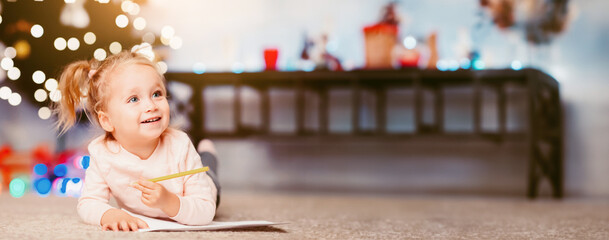 Wall Mural - Drawing Xmas greeting card. Little girl lying on floor near Christmas tree at home