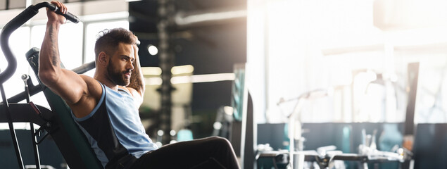 Wall Mural - Healthy lifestyle and sport concept. Young man exercising with training apparatus in gym, empty space