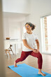 © insta_photos - Sporty fit middle aged woman standing on mat at home doing fitness exercises morning routine. Happy healthy mature 50 years old lady enjoying casual workout or yoga in living room, vertical photo.