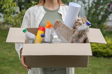 Sticker - Recycling. Woman holding cardboard box with different garbage outdoors, closeup