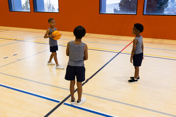 Playing basketball in school gym, three multiracial boys practicing together on court