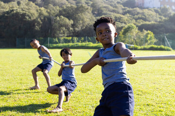 playing tug of war, multiracial boys enjoying outdoor activity at school field