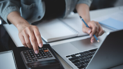 Close up business woman hand using calculator to calculate home finance, accounting with laptop computer on table, budget management, monthly expenses. Doing finance, budgeting and tax calculation