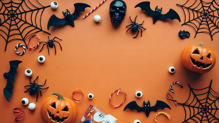 This image presents a Halloween-themed flat lay on an orange background. The arrangement features classic spooky decorations, including black plastic bats, spiders, and spiderwebs, along with eyeball 