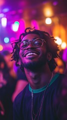 A young, multicultural man dressed in a chic black and green t-shirt dances against his pals and the deejay in a purple neon-lit nightclub.