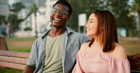 Laughing, love and couple on bench in park for outdoor fun, bonding and care with interracial relationship. Romance, happy man and woman on date with smile, relax and calm weekend holiday together