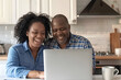 © Aleena - Black senior couple using laptop in kitchen at home, smiling and looking happy together while watching video on computer screen. A feeling of warmth and love between two people