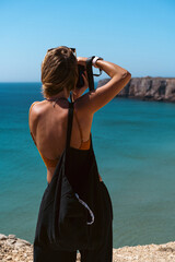 Woman traveler takes pictures with a camera on the beach.