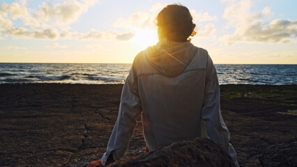 Wall Mural - Man on a beach is looking distance during beautiful summer sunset. Human looks to the sun over horizon in the morning while sunrise. Happy person contemplates the beauty of nature. Freedom concept.