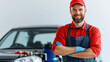© khonkangrua - A smiling auto mechanic with arms crossed, standing confidently in a garage with a car in the background.