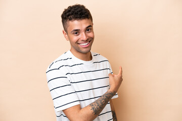 Young Brazilian man isolated on beige background pointing back