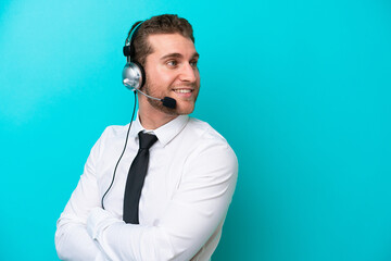 Wall Mural - Telemarketer caucasian man working with a headset isolated on blue background with arms crossed and happy