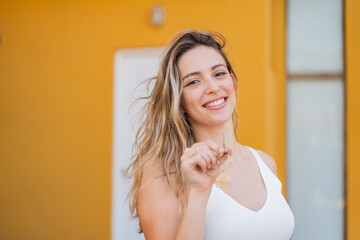 Wall Mural - Young pretty woman holding home keys at outdoors with happy expression