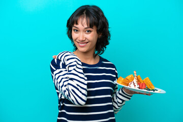 Sticker - Young Argentinian woman holding waffles isolated on blue background laughing