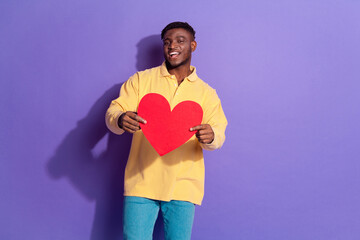 Photo portrait of handsome young guy hold heart postcard dressed stylish yellow garment isolated on violet color background