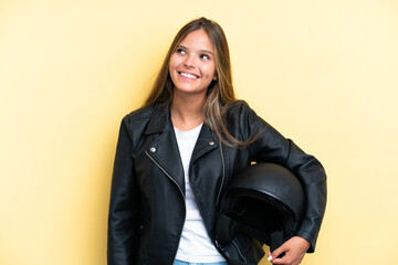 Young caucasian woman with a motorcycle helmet isolated on yellow background thinking an idea while looking up