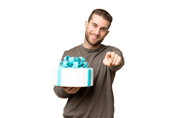 Young handsome blonde man holding birthday cake over isolated chroma key background pointing front with happy expression