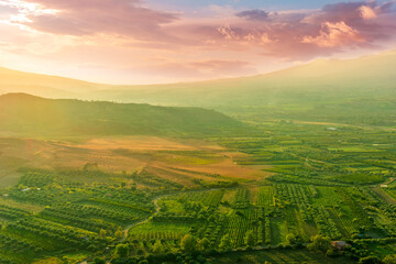 scenic rustic landscape with green hills and farms in a mountain valley during colorful cloudy sunset