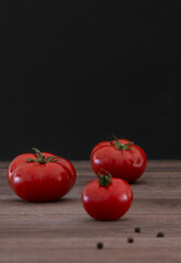 Tomatoes on a wooden table, black background, copy space.