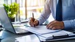 © bteeranan - Businessman signing documents at desk with laptop