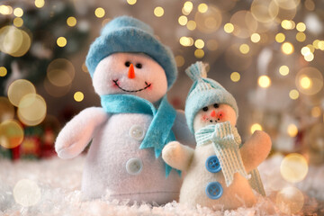 Wall Mural - Cute snowmen against blurred Christmas lights, closeup. Bokeh effect