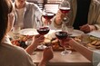 © New Africa - People clinking glasses of red wine at served table, closeup