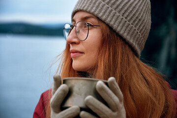 Pretty smiling female traveler drinking from thermos outdoors