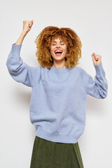 Happy woman celebrating success in light blue sweater, with curly hair and joyful expression against a plain white background Energetic and positive vibes radiate from the image