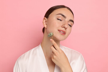 Poster - Beautiful young woman doing facial massage with roller on pink background