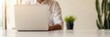 © Vilaysack - Business professional in a white shirt works on a laptop in a well-lit office with natural sunlight and minimalistic decor, including a small plant in the background.