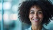 © Dulemegapixel - A radiant woman smiles brightly, exuding natural joy in an indoor setting. Her welcoming expression and afro hairstyle are highlighted by the gentle ambient light.