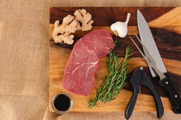 Raw beef steak with ginger root, garlic, soy sauce, and rosemary close-up on a wooden cutting board