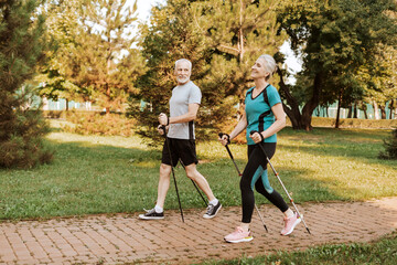 Smiling senior woman and man wearing sportwear enjoying nordic walking exercise together in park