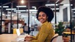 © Felippe Lopes - Smiling Black woman in a yellow shirt works on her laptop at her desk in a modern office.