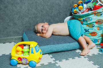 A little boy in shorts sits on the carpet at home and plays with educational toys. A child builds a plastic pyramid.