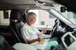 © Davor - Senior nurse eating lunch in car and using smartphone